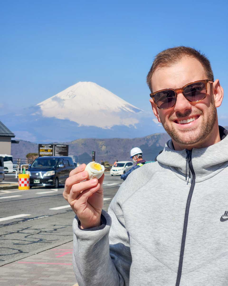 Daniel-eats-a-black-egg-with-Fuji-in-the-background-at-Owakudani-Hakone-Japan-on a tour from Tokyo